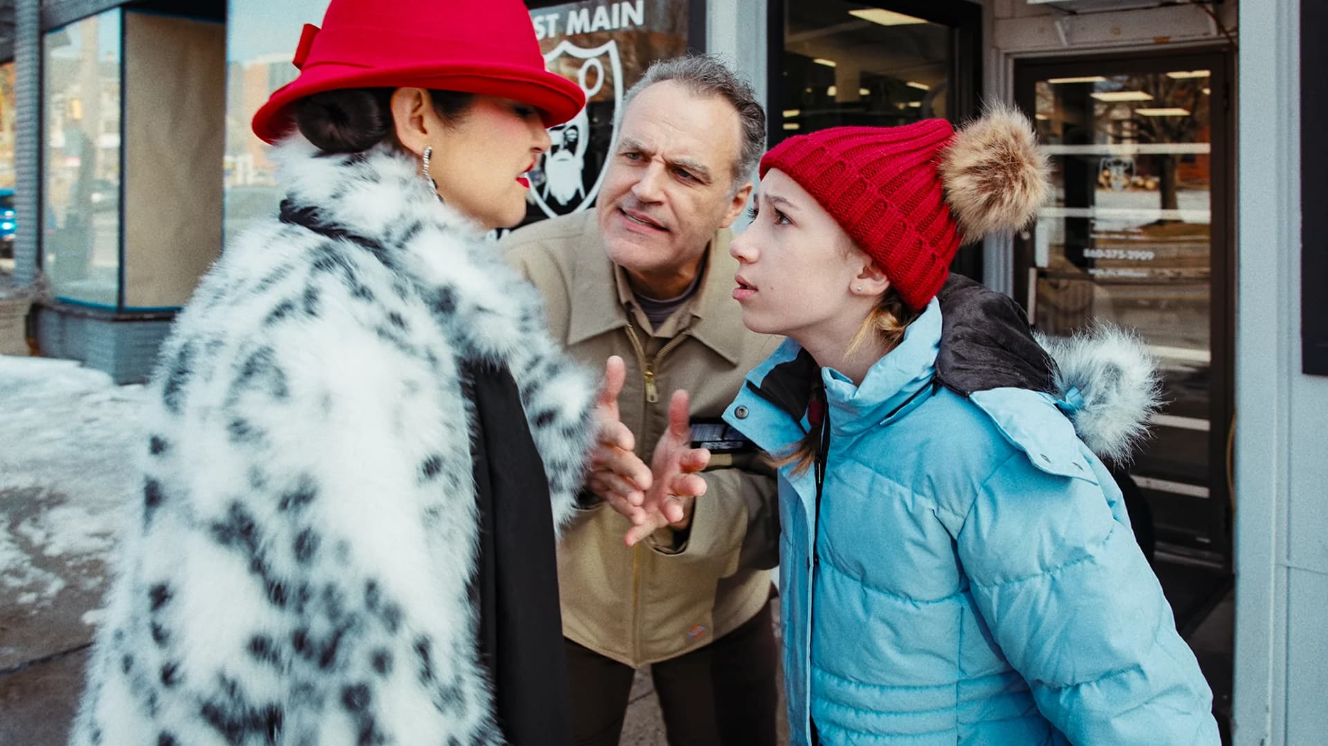 A girl in a red knit hat and a man in a work jacket plead with a woman in a spotted fur coat on a snowy sidewalk in Not My Dog